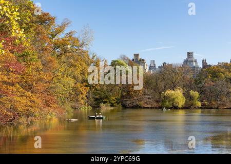 Ein ruhiger See spiegelt im Herbst im Central Park leuchtende Herbstfarben wider. Besucher in der ruhigen Atmosphäre unter einem hellblauen Himmel. Stockfoto