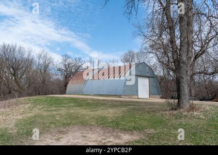 Rustikales Quonset in ruhiger Landschaft mit klarem blauem Himmel und umliegenden Bäumen. Stockfoto