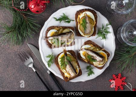 Hausgemachte warme Sandwiches mit Sprotten, Ei, Käse und eingelegter Gurke auf rundem Teller mit braunem Hintergrund Stockfoto