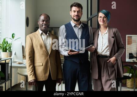 Gruppe von drei erfolgreichen interkulturellen Maklern in Formalwear mit Blick auf die Kamera im modernen Coworking Space Stockfoto