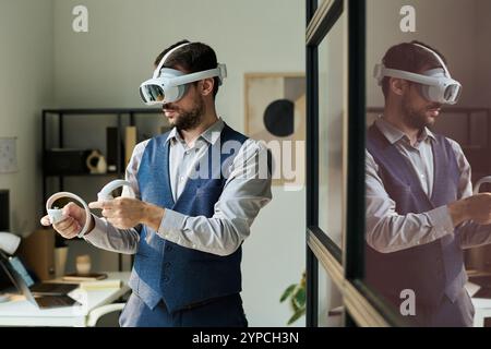 Geschäftsmann, der ein VR-Headset trägt und die Tasten auf den Fernbedienungen drückt, während er das neue Projekt vorstellt Stockfoto