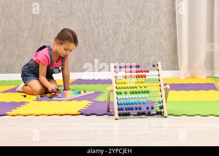 Autismustherapie. Kleines Mädchen, das mit pädagogischem Spielzeug auf dem Boden im Zentrum für psychische Gesundheit spielt, Fokus auf Abacus Stockfoto