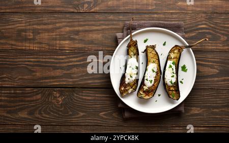 Gebackene Aubergine mit Knoblauch-Joghurt-Dressing auf Teller über hölzernem Hintergrund mit freiem Platz. Draufsicht, flach Stockfoto