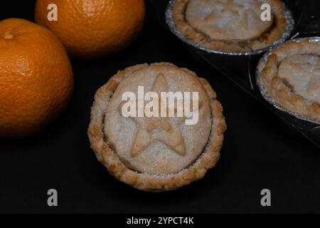 Zitrusfrüchte und frisch gebackene Hackkuchen mit Sternsymbol auf dunklem Hintergrund Stockfoto