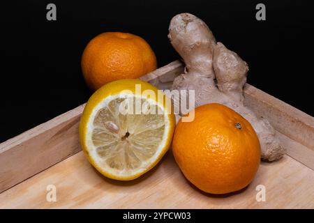 Zitrusfrüchte mit Ingwerwurzel auf Holztablett mit schwarzem Hintergrund, natürliche Gesundheitsunterstützung, entzündungshemmende Mittel und Lebensmittel Stockfoto