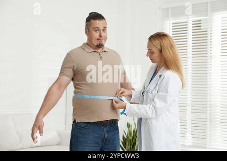 Ernährungswissenschaftler, der die Taille eines übergewichtigen Mannes mit Klebeband in der Klinik misst Stockfoto