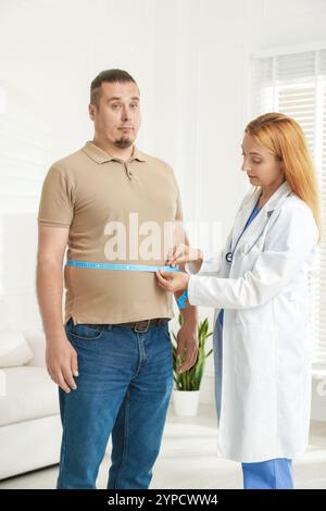 Ernährungswissenschaftler, der die Taille eines übergewichtigen Mannes mit Klebeband in der Klinik misst Stockfoto