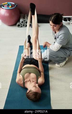 Fitnesstrainer unterstützt Kunden beim Dehnen auf Yogamatte im Fitnessstudio, fördert die körperliche Gesundheit und die Flexibilität des Körpers Stockfoto
