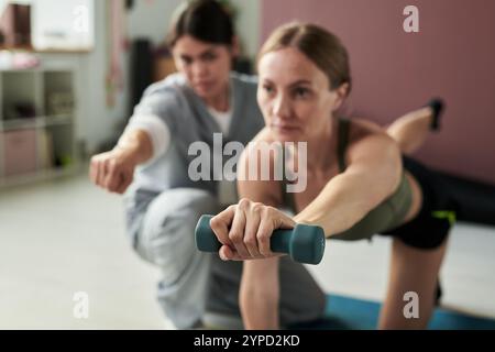 Frauen, die in einem Fitnessstudio mit Fokus und Hingabe die Hanteln heben. Fitnessgeräte im Hintergrund vorhanden Stockfoto