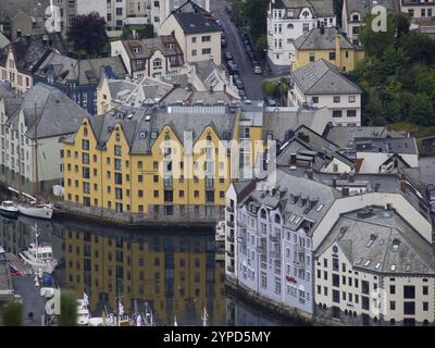 Gelbe und weiße Häuser spiegeln sich im Kanal wider, umgeben von mehreren kleinen Booten, alesund, norwegen Stockfoto