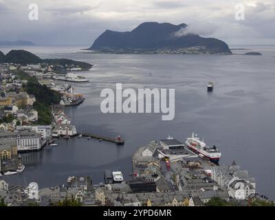 Hafenstadt mit mehreren Schiffen und einer Bergkulisse unter einem bewölkten Himmel, alesund, norwegen Stockfoto