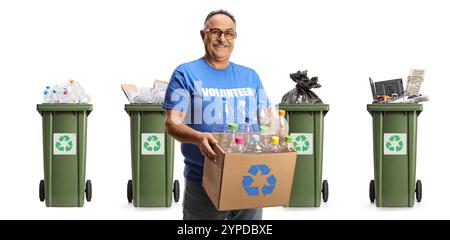 Fröhlicher, reifer Freiwilliger, der eine Kiste mit Plastikflaschen zum Recycling vor Mülltonnen auf weißem Hintergrund hält Stockfoto