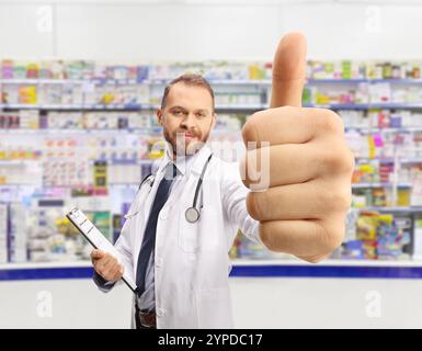 Ein Chemiker hält ein Klemmbrett und drückt die Daumen in einer Apotheke nach oben Stockfoto