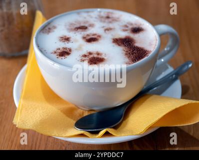 Tallinn, Estland - 16. August 2024: Gelbe Tasse Kaffee in einem Katzencafé. Der Schaum des Getränks zeigt einen Katzen- und Pfotenabdruck, selektiv fokussiert Stockfoto