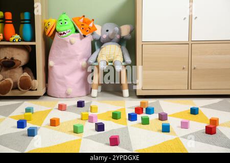 Bunte Würfel auf Teppich und verschiedene Spielzeuge im Kinderzimmer Stockfoto