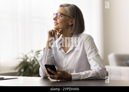 Glückliche, nachdenkliche freiberufliche Frau, die am Arbeitstisch sitzt Stockfoto
