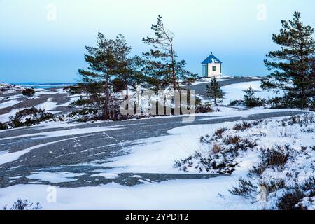 Schneebedecktes Gelände mit Kiefern und einer kleinen weißen Hütte unter einem weichen blauen Himmel. Friedliche Winterszene mit natürlicher Schönheit, perfekt für saisonale Backups Stockfoto