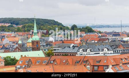 Aus der Vogelperspektive von Aarhus, Dänemark, mit traditionellen roten Dächern, dem grünen Kirchturm und einer üppigen, bewaldeten Kulisse, mit der Uferpromenade im Th Stockfoto