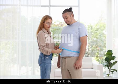 Ernährungswissenschaftler, der die Taille eines übergewichtigen Mannes mit Klebeband in der Klinik misst Stockfoto