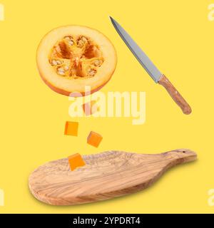 Stücke von frischem rohen Kürbis und Messer in der Luft über Holzbrett auf goldenem Hintergrund Stockfoto