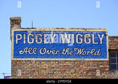 Helper, UT, USA - 11. Juni 2024; Blaues Schild für Piggly Wiggly in der ganzen Welt an der alten Ziegelsteinmauer Stockfoto