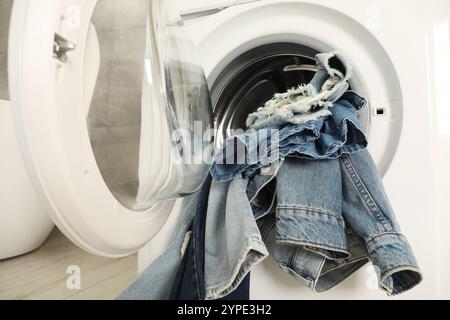 Waschmaschine mit schmutzigen Jeans und anderen Denim-Kleidern im Innenbereich Stockfoto