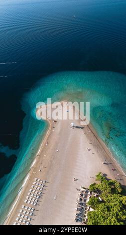 Ein atemberaubender Blick auf den Strand von Zlatni Rat zeigt seine einzigartige Form und das atemberaubende türkisfarbene Wasser. Besucher genießen die Sonne auf weichem Sand und schaffen eine lebendige Atmosphäre in diesem kroatischen Paradies. Stockfoto