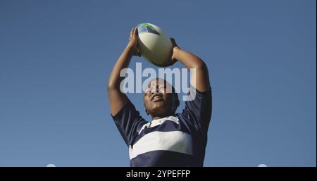 Vorderansicht des unteren Winkels einer jungen erwachsenen, birassischen Rugbyspielerin, die den Ball schreit und hinwirft Stockfoto