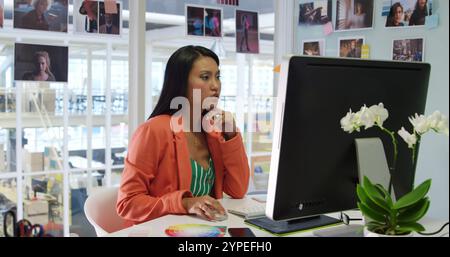 Vorderansicht einer jungen, birassischen Unternehmerin, die in einem modernen Büro arbeitet, mit einem Computer Stockfoto