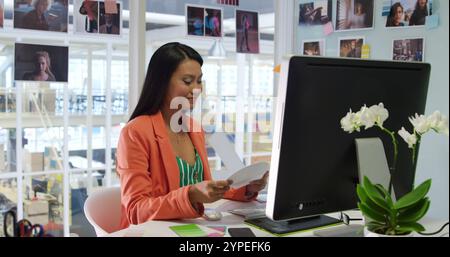 Vorderansicht einer jungen, birassischen Unternehmerin, die in einem modernen Büro arbeitet, mit einem Computer Stockfoto