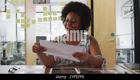 Lächelnde afroamerikanische Geschäftsfrau am Schreibtisch, die während eines Telefongesprächs im Büro ein Bild zeigt Stockfoto