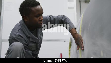 Afroamerikaner, männlicher Automechaniker, der in einer Township-Werkstatt arbeitet und eine Seite eines Autos poliert Stockfoto