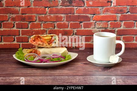 Köstliche saftige Fleisch-Shawarma mit Salat und roten Zwiebeln auf einem Holztisch, neben einer Tasse heißen Tee. Nahaufnahme. Stockfoto