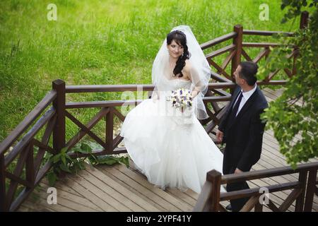 Braut mit Blumenstrauß, die Holztreppen hinuntergeht, mit Bräutigam in einer Hochzeitszeremonie im Freien Stockfoto