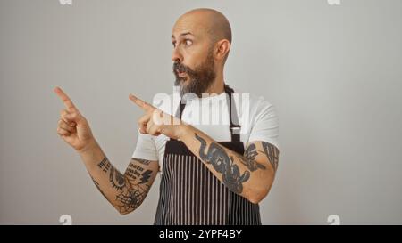 Überraschter hispanischer Mann mit Bart und Tätowierungen, die schockiert vor weißem Hintergrund zeigen Stockfoto