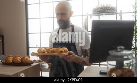 Kahler hispanischer Mann, der ein Tablett mit Gebäck in einer Bäckerei mit Fensterbeleuchtung und einer Ausstellungstheke hält Stockfoto