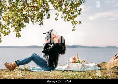 Mutter genießt die schöne Zeit mit ihrem Baby während eines entspannenden Picknicks am See im Schatten eines Baumes Stockfoto