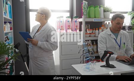 Frau und Mann Apotheker arbeiten in einer Apotheke, die Frau überprüft die Regale und der Mann benutzt einen Laptop an der Theke Stockfoto