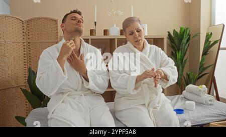 Mann und Frau genießen Entspannung in einem Spa, tragen weiße Bademäntel und tragen gleichzeitig Hautpflegeprodukte auf und präsentieren eine ruhige Wellness-Einrichtung Stockfoto