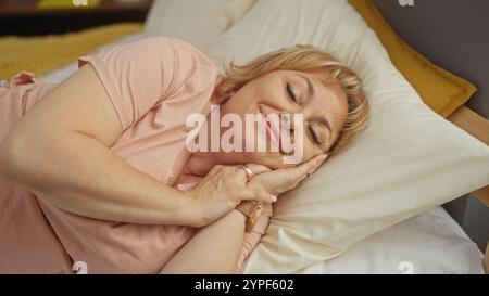 Eine ältere kaukasische Frau entspannt sich zufrieden in einem komfortablen Bett zu Hause und bietet ein friedliches Innenleben und eine ruhige Ruhe in einem Schlafzimmer. Stockfoto