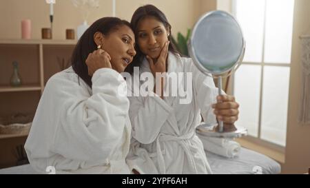 Mutter und Tochter in weißen Bademänteln teilen sich einen schönen Moment, während sie in einem gemütlichen Spa-Ambiente drinnen in einen Spiegel blicken Stockfoto