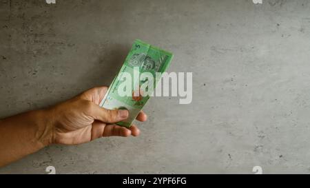 Ein Mann mit 5 malaysischen Ringgit-Banknoten vor einem konkreten Hintergrund, der sich auf südostasiatische Währungen und Finanzkontexte konzentriert. Stockfoto