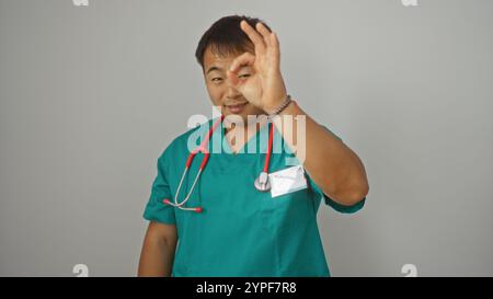 Junger, gutaussehender, chinesischer männlicher Doktor in grünen Peelings und rotem Stethoskop mit Gesten OK-Zeichen, isoliert auf weißem Hintergrund. Stockfoto