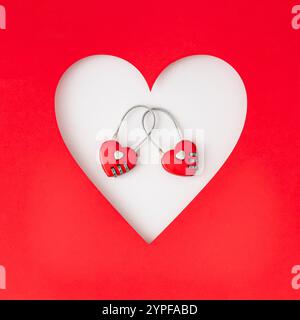 Romantisches Layout mit rotem, herzförmigem Gepäckvorhängeschloss auf weißem und rotem Hintergrund. Minimales kreatives Liebeskonzept. Zum Valentinstag flach liegend. Stockfoto