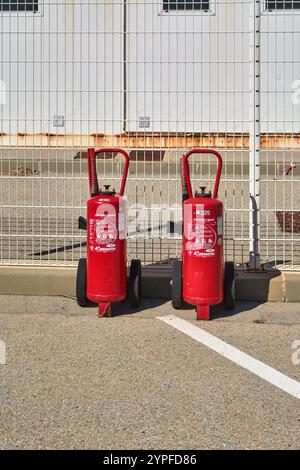Marseille. Frankreich - 30. November 2024: Zwei große, rote Feuerlöscher auf Rädern stehen in der Nähe eines Drahtzaunes einsatzbereit Stockfoto