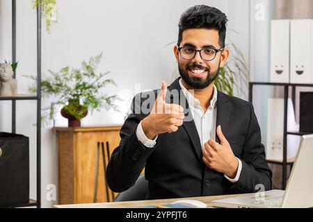 Gefällt Mir. Glücklicher indischer Geschäftsmann, der am Laptop arbeitet, der zustimmend in die Kamera schaut und Daumen nach oben zeigt, wie Zeichen positives etwas gutes, positives Feed Stockfoto