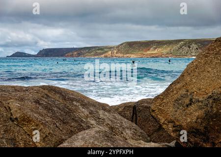 Surfer im Meer in Sennen Cove an einem herbstlichen Tag mit der Küste im Hintergrund Cornwall England UK Stockfoto