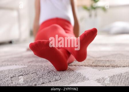 Kind in roten Strumpfhosen sitzt zu Hause auf dem Boden, Nahaufnahme Stockfoto