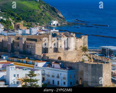 Das mittelalterliche Castillo de Guzman el Bueno steht mit Steinmauern und Zinnen, umgeben von weiß getünchten andalusischen Gebäuden und üppigen grünen Hügeln Stockfoto