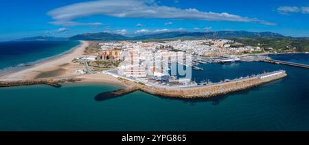 Tarifa, Spanien, ist von oben gesehen, mit einem Sandstrand, pulsierendem blauem Wasser, einem Hafen mit Booten, weiß getünchten Gebäuden und fernen Bergen. Stockfoto